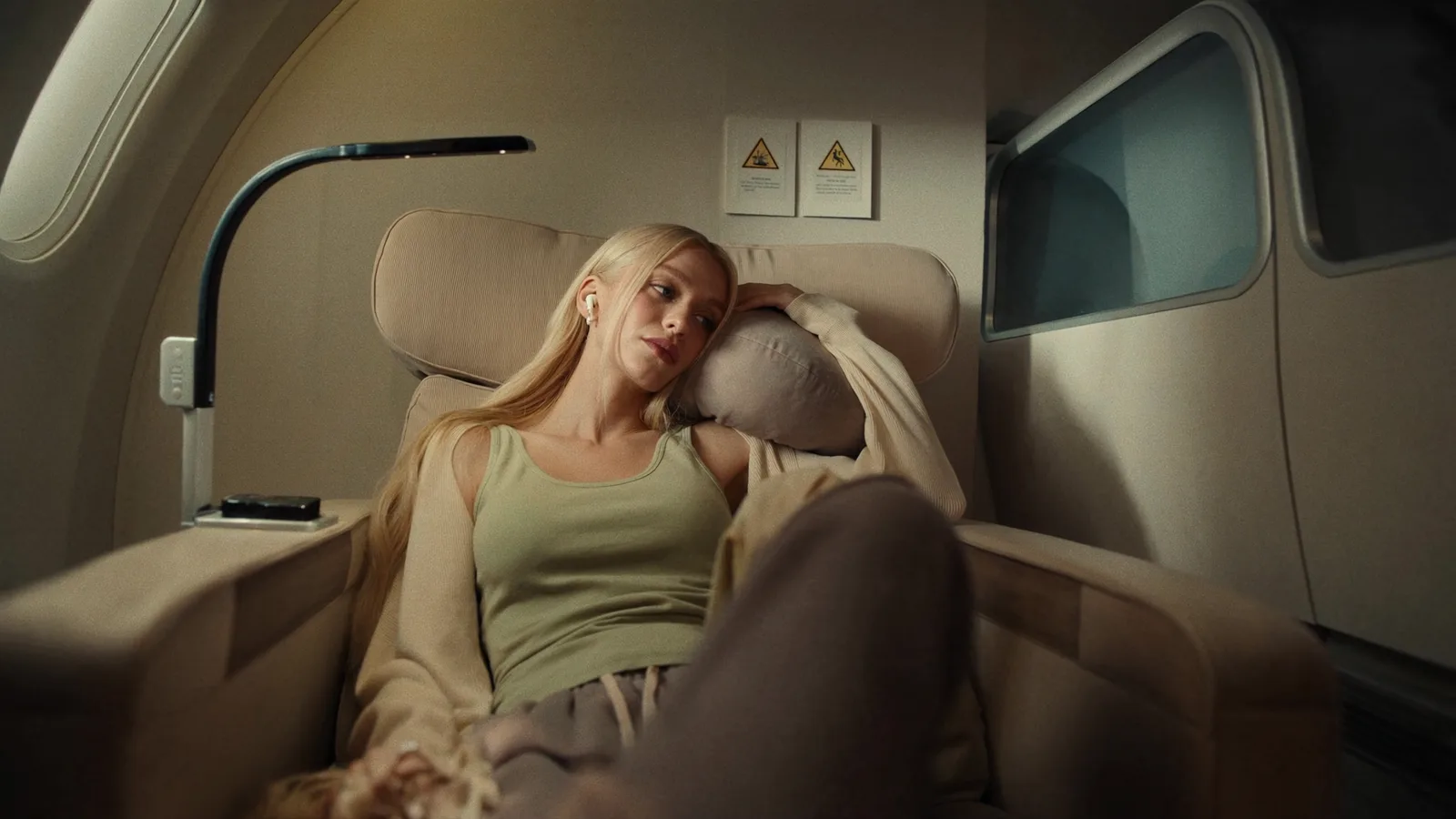 A traveler relaxing in a plane seat with earbuds in, head resting on a pillow